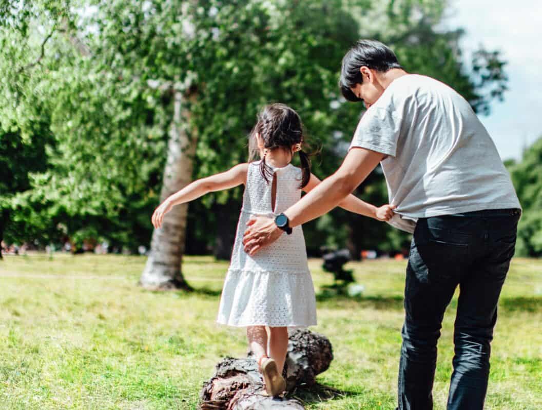 man helping his daughter walk on a log