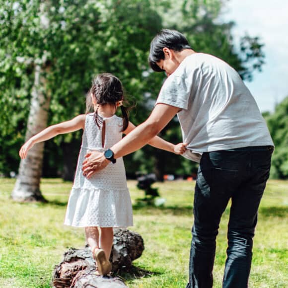 man helping his daughter walk on a log